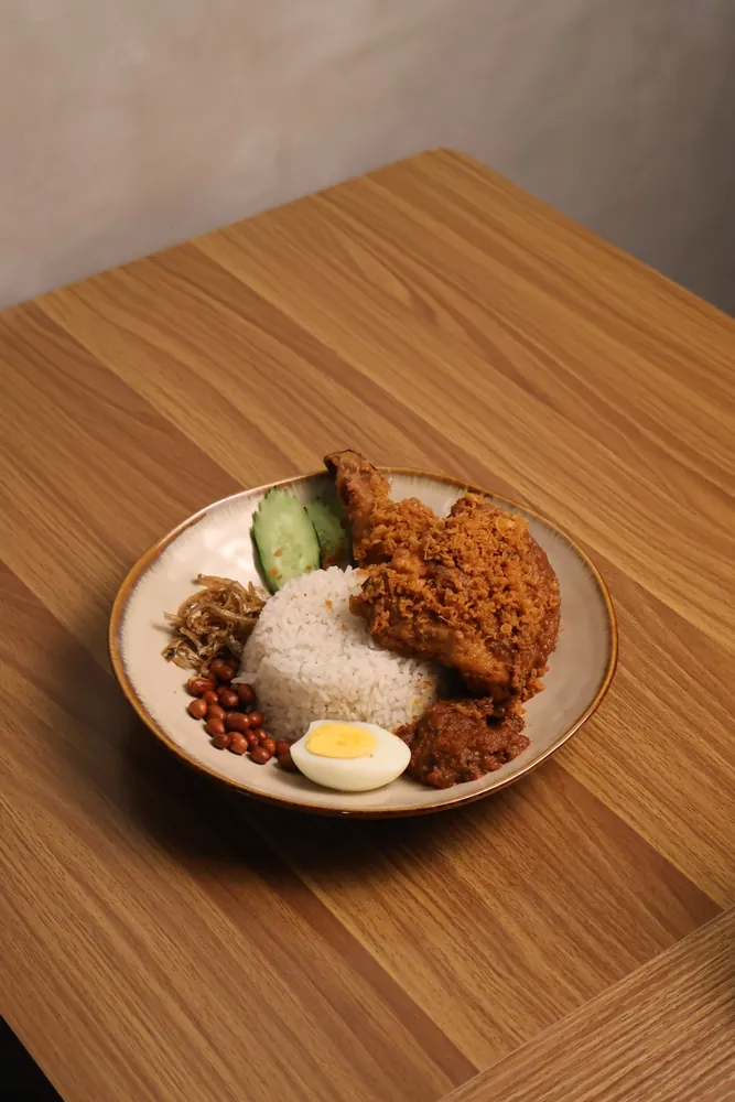 A plate of nasi lemak: coconut rice, spiced fried chicken, sambal, fried anchovies, roasted peanuts, a halved boiled egg and cucumber